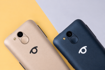 Detail dvou telefonů BlindShell Classic 3 v barvách Zlatavě pískové a Oceánově modré, umístěných vedle sebe na jemně žlutém a světle šedém pozadí. Oba telefony jsou zobrazeny zezadu s důrazem na fotoaparát, blesk, kulaté SOS tlačítko a logo BlindShell.