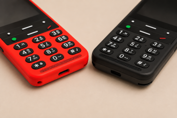 Detail dvou telefonů BlindShell Classic 2 v červené a černé barvě, umístěných vedle sebe na teplém béžovém pozadí. Snímek se zaměřuje na jejich velké hmatové klávesnice s dobře rozlišitelnými tlačítky, mřížky reproduktorů a nabíjecí konektory.